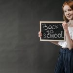 Young girl holding a 'Back to School' chalkboard, ready for the school year.